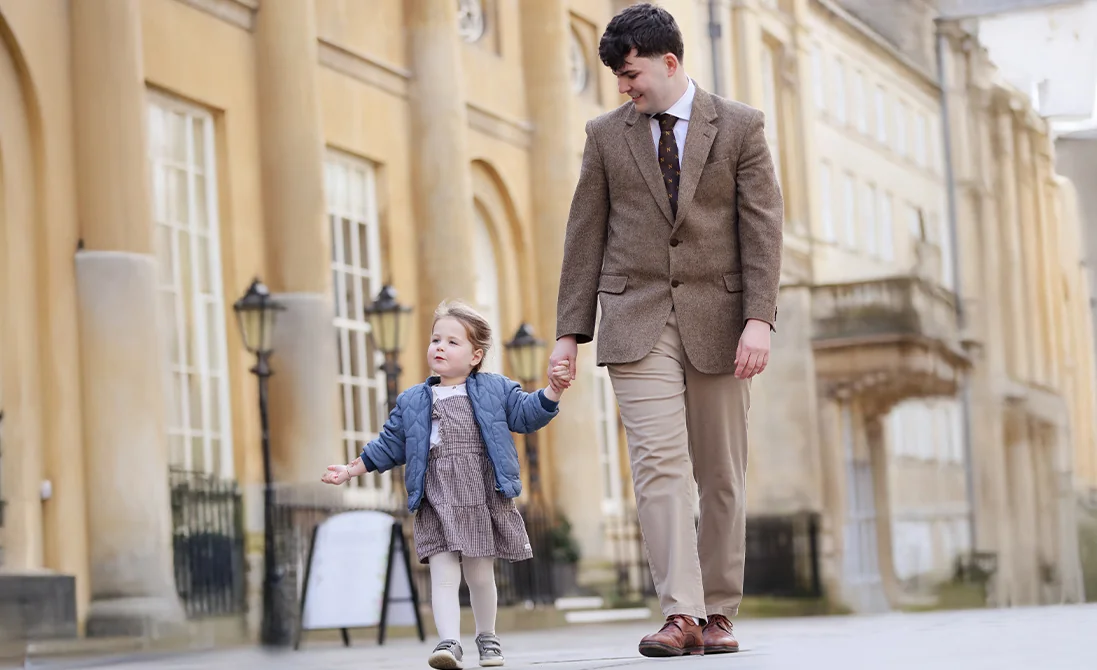 A male Norland Nanny walking through Abbey Churchyard with a child