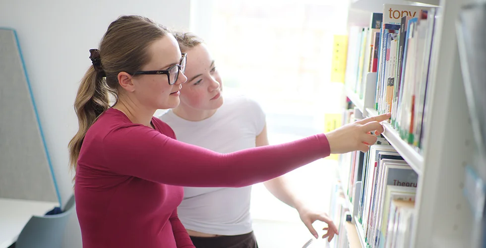 Two students looking at some books on a bookshelf in a library