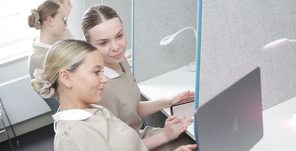 A female Norland Nanny student showing her laptop screen to another student in the library at the Oldfield Park campus