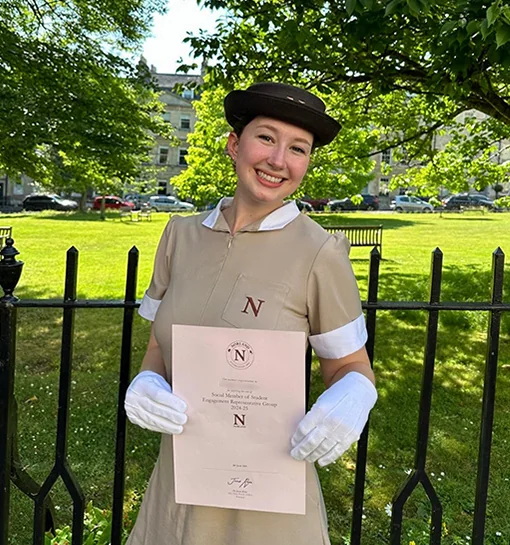 Student in uniform holding certificate in front of park