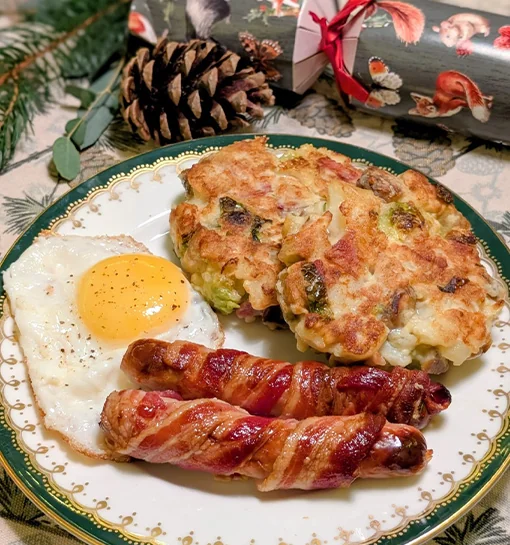 Some sausages, an egg and bubble and squeak on a festive dinner table