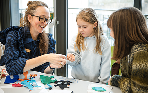 Sewing lecturer with child and parent demonstrating sewing technique