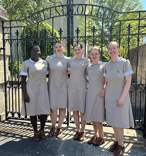 Norland students in uniform smiling outside of gates