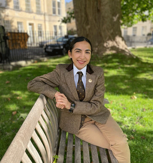Norland student in uniform sat on bench in sunny park smiling