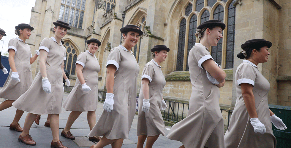 Norland graduates in uniform walking by Bath Abbey