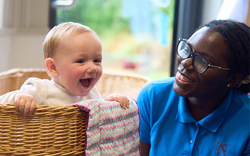 A Norland Nanny student in her practical uniform smiling with a child